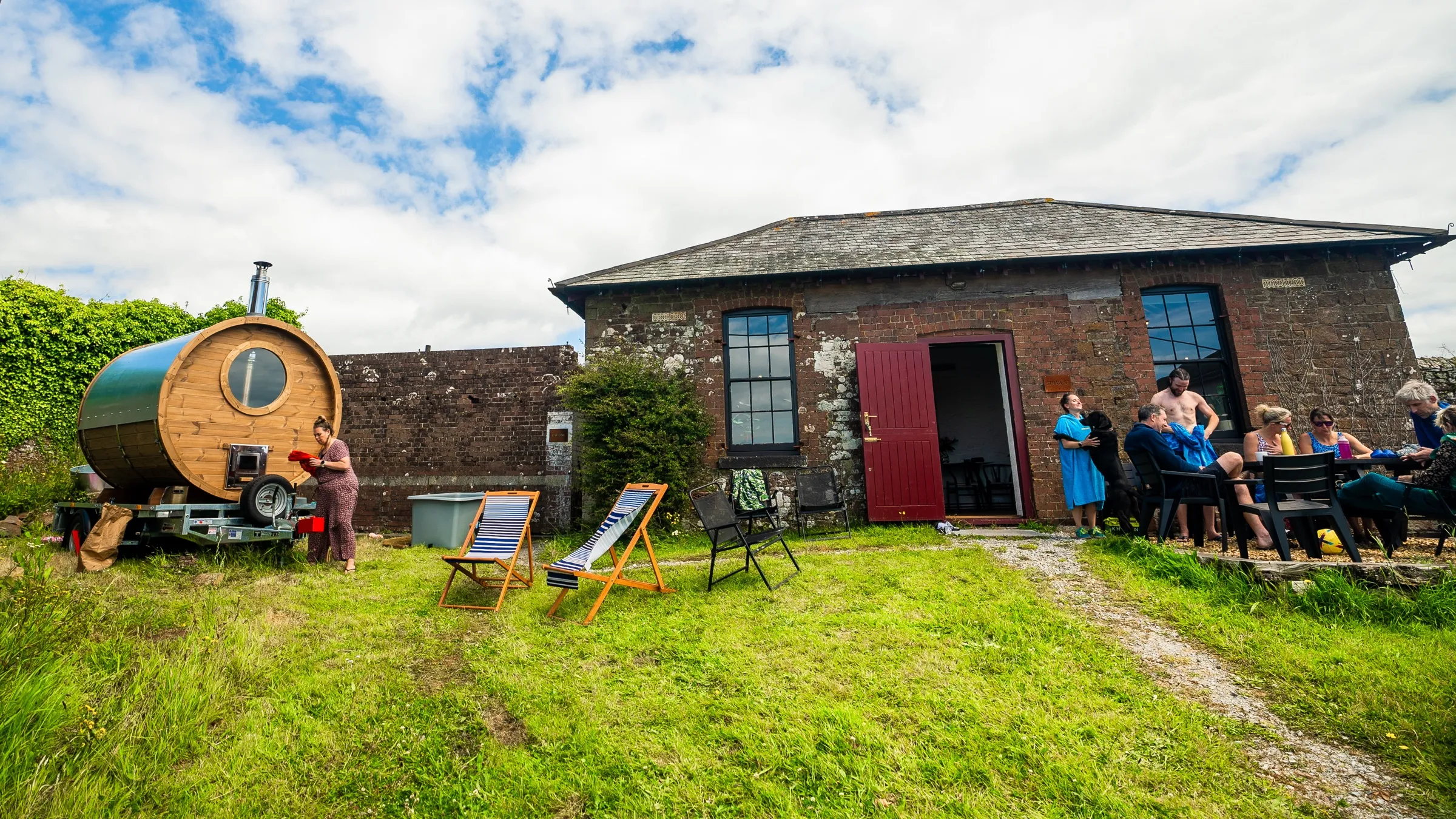 The Lit barrel sauna beside the Straw Store at Maker Heights, with guests relaxing on the grass
